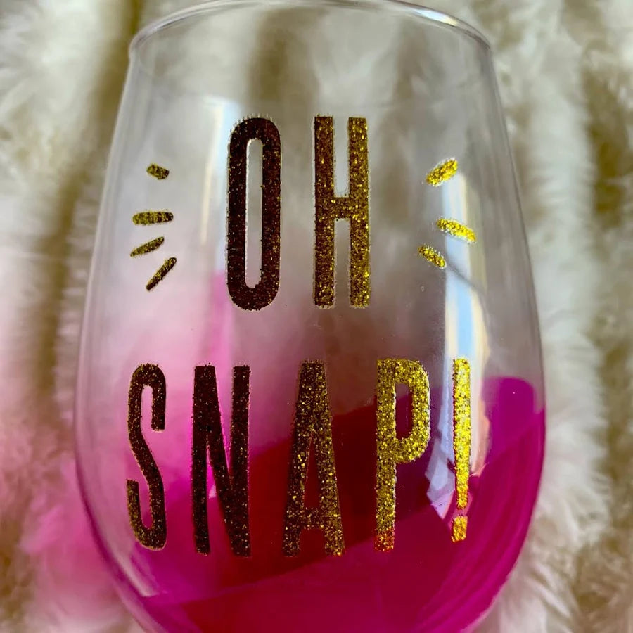 A stemless wine glass with a pink-to-clear gradient and glittery gold text reading 'OH SNAP!'.