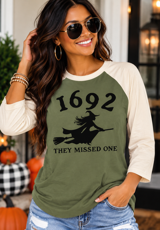Woman wearing the Southern Script 1692 They Missed One Halloween raglan in military green and cream with a black witch design.
