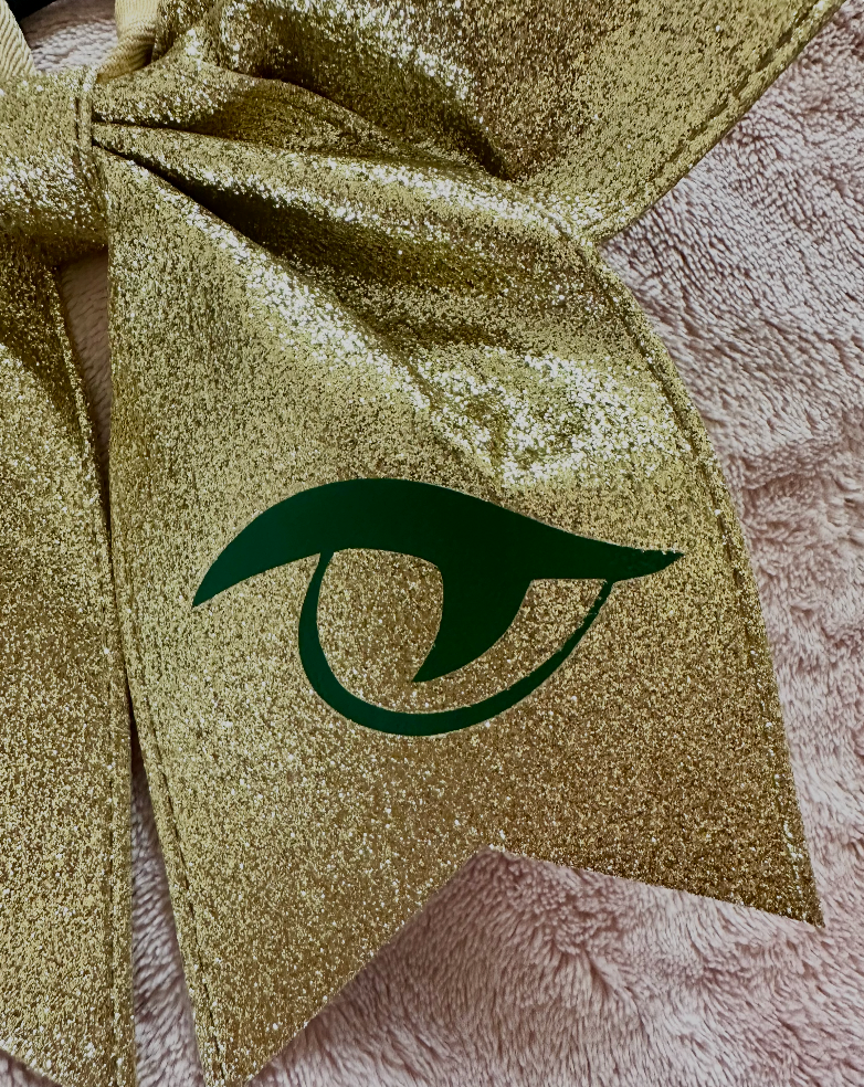 Close-up detail of gold glitter with matte green Gator Eye vinyl logo grosgrain River Bluff cheer bow tail