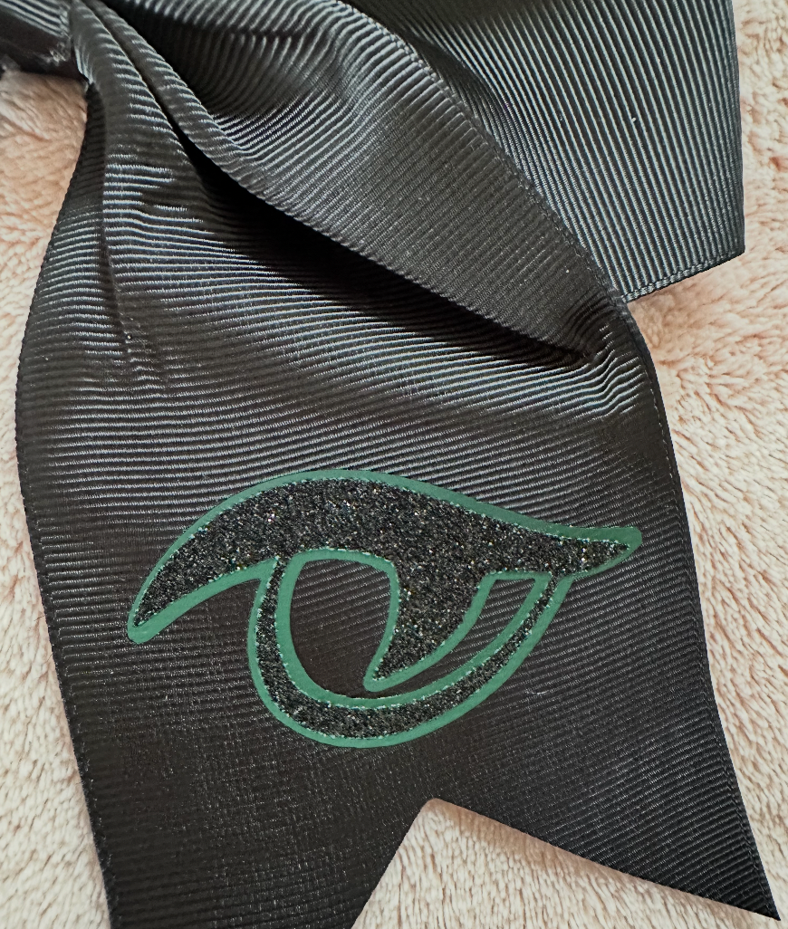 Close-up detail of matte green and black glitter Gator Eye vinyl logo on black grosgrain River Bluff cheer bow tail