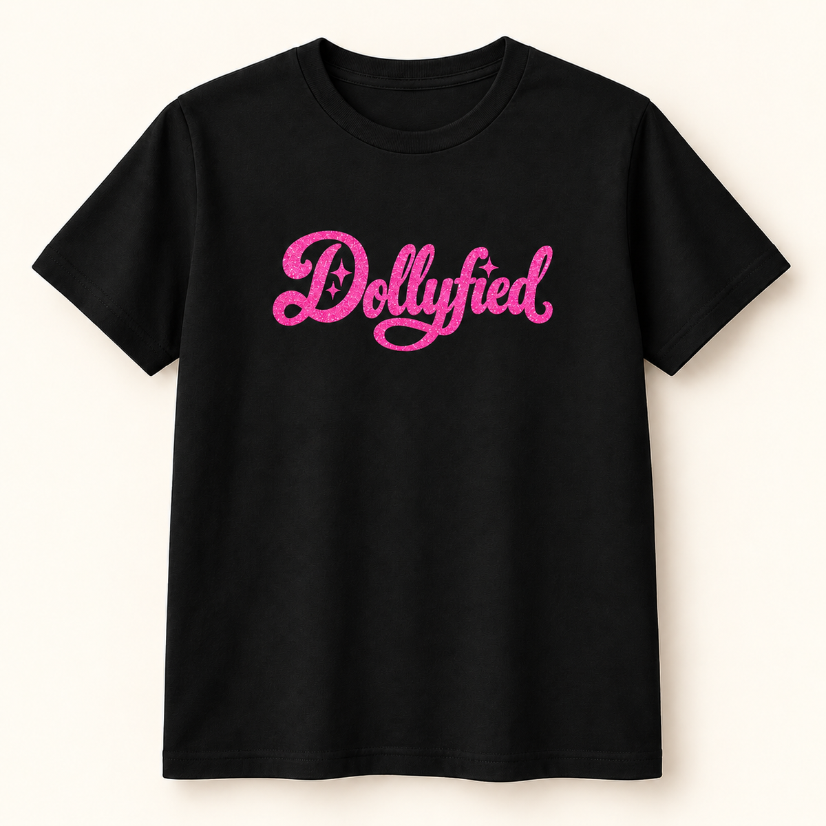 A black short-sleeve crewneck t-shirt featuring the word 'Dollyfied' printed across the chest in a vibrant pink cursive font with small star accents, displayed against a light cream background.