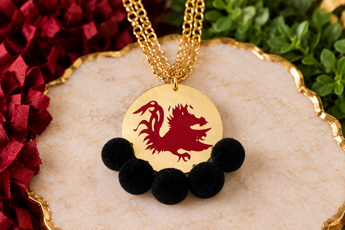Carolina Gamecock Pom Pom Statement Necklace by Southern Script with Black pom poms, garnet Gamecock design and matte-gold round pendant.