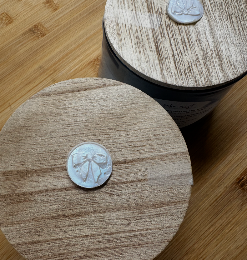Close-up of the light wood lid and iridescent bow wax seal on a Murray Moments Lake Mist candle