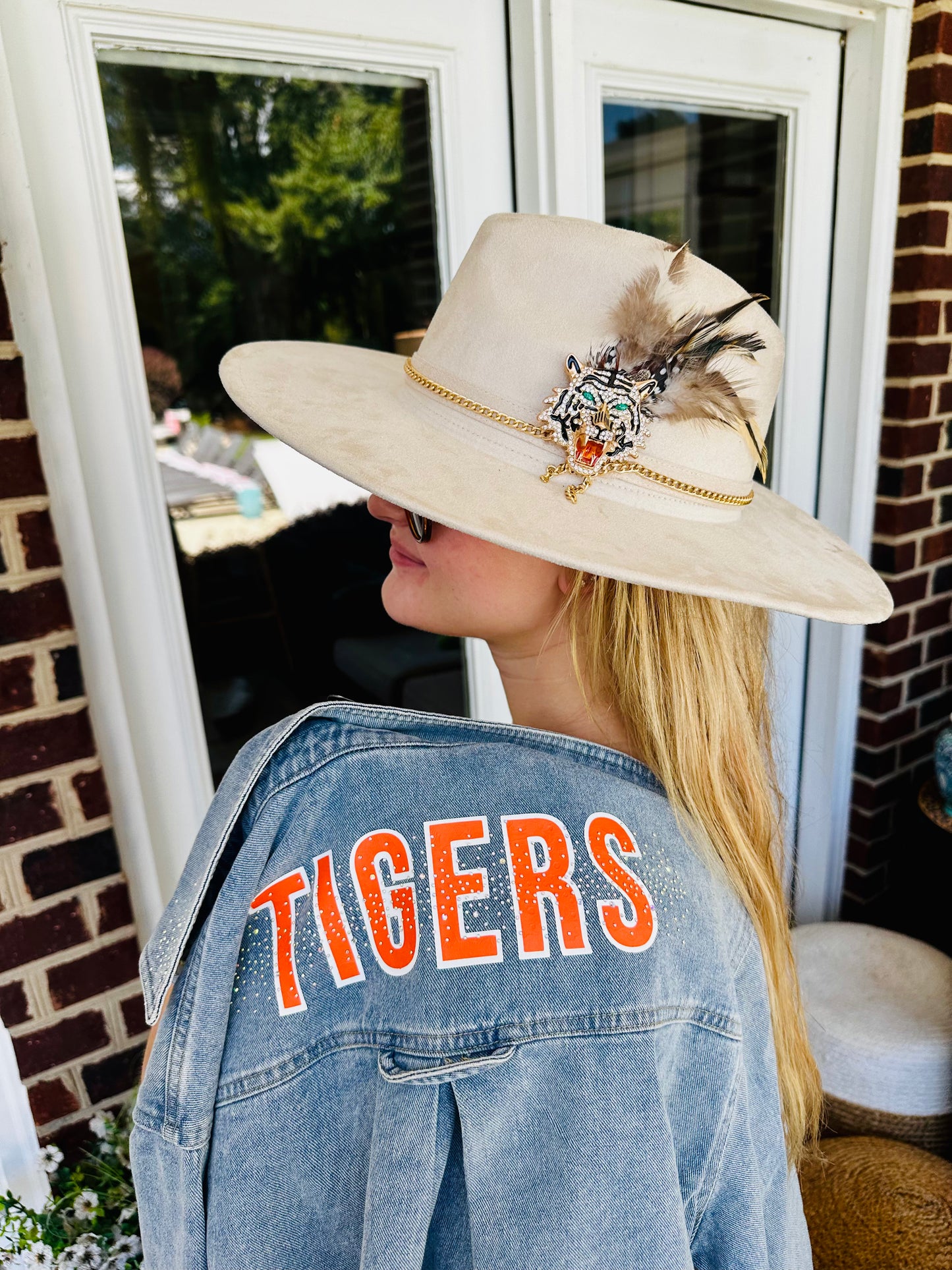 Woman wearing a cream Clemson Show Stopping Topper with jeweled tiger, gold chain and feather accents over a TIGERS denim jacket.