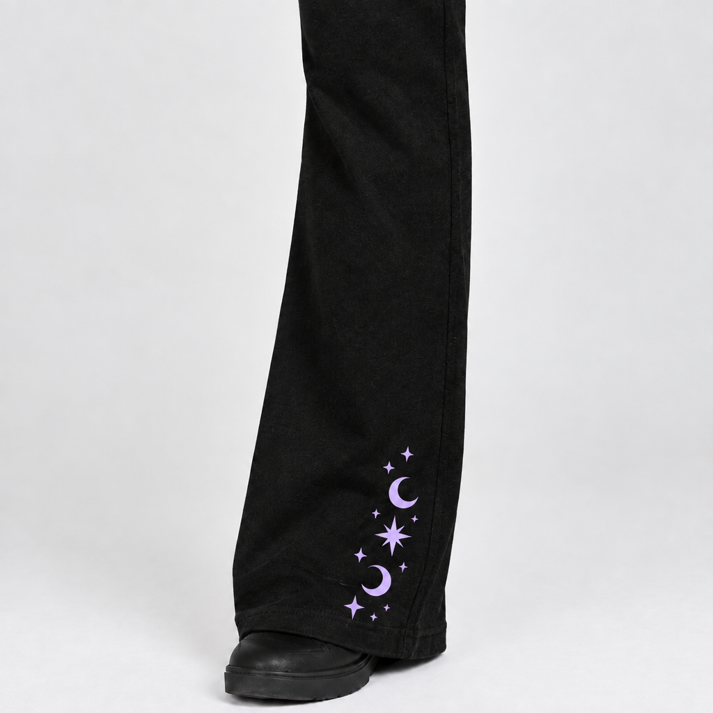Close-up of the model's left black pant leg with lavender crescent moons and stars confined to the lower leg near the hem.