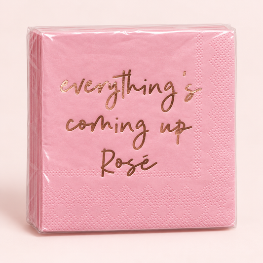 A stack of pink paper napkins wrapped in clear plastic, featuring the phrase 'everything's coming up Rosé' printed in metallic rose gold script on the front.