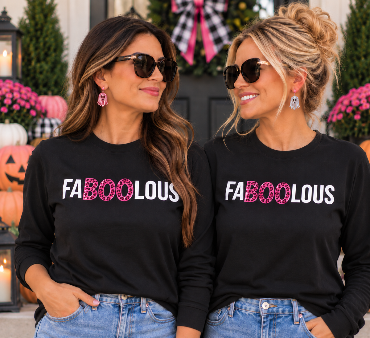 Two women wearing matching black long-sleeve crewneck t-shirts with 'FABOOLOUS' printed across the chest in white and pink glitter-style lettering, posed outdoors in front of Halloween decorations.