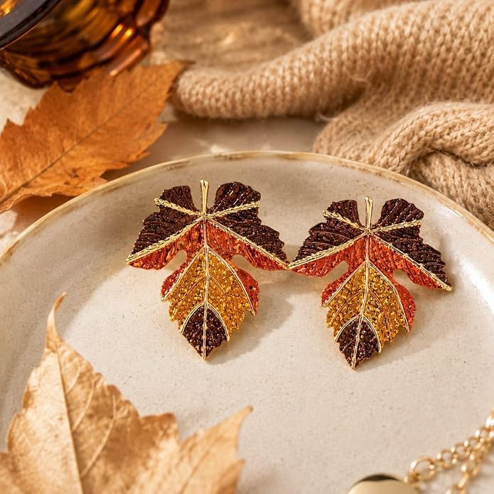 Pair of multicolor brown, orange and gold-tone maple leaf dangle earrings displayed on a tray