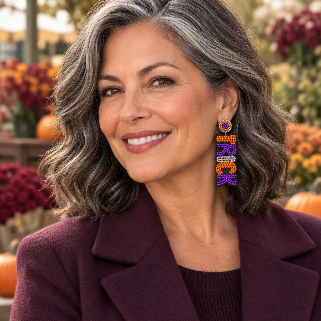 Middle-aged woman with salt-and-pepper hair wearing the stacked orange, purple, silver, and black TRICK beaded earrings in an autumn market setting.