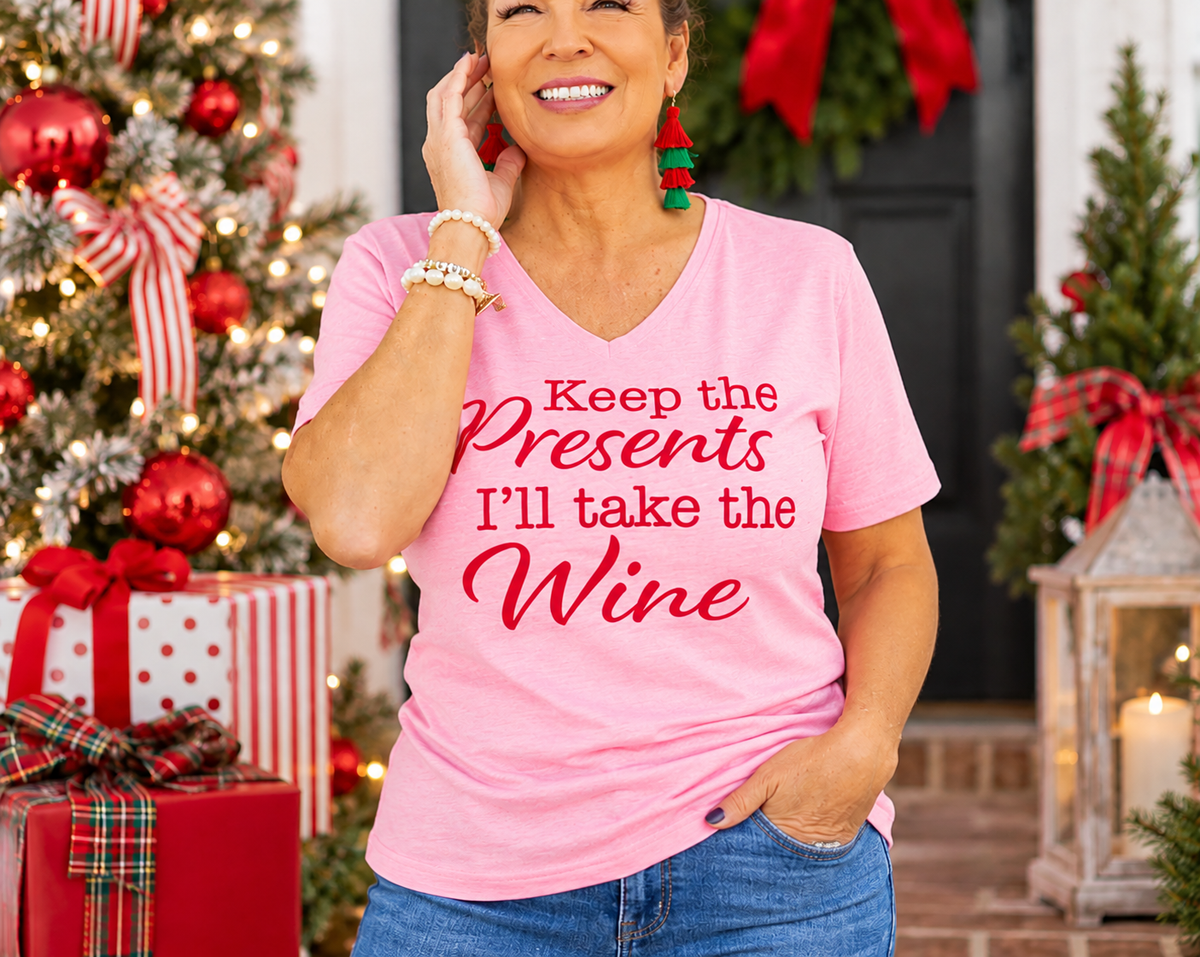 Pink Keep the Presents, I’ll Take the Wine V-neck tee with red lettering, styled with jeans in a Christmas setting